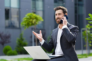 Man sat outside on phone with laptop